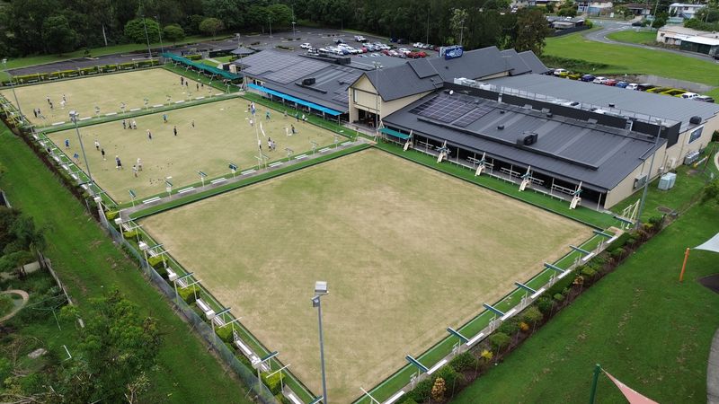Aerial view of the clubhouse and its three bowling greens, with bowlers on the far green